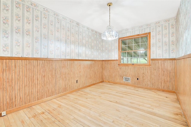 empty room featuring wood-type flooring, a chandelier, wainscoting, and wallpapered walls