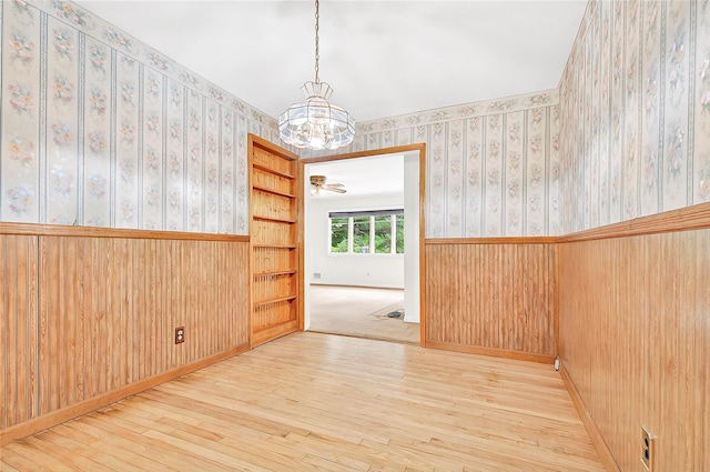 spare room featuring a chandelier, wood-type flooring, wainscoting, wallpapered walls, and wooden walls