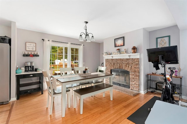 dining space with light wood finished floors, a chandelier, a fireplace, and baseboards