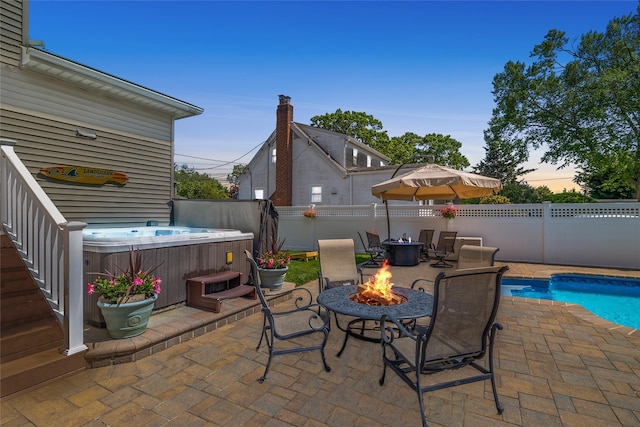 patio terrace at dusk featuring an outdoor fire pit, a hot tub, and a fenced backyard
