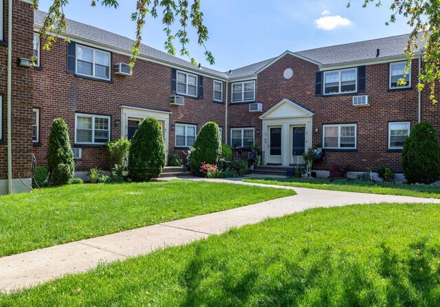 townhome / multi-family property featuring a front lawn, brick siding, and a wall unit AC