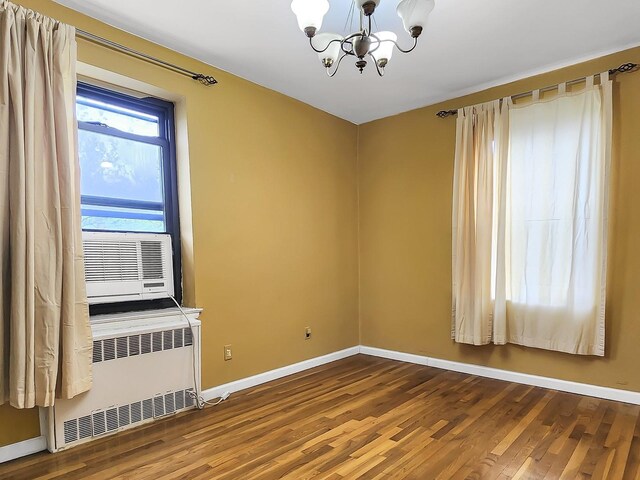unfurnished room with radiator heating unit, a chandelier, wood finished floors, and baseboards
