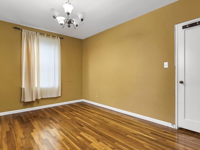 spare room with baseboards, wood finished floors, and a chandelier