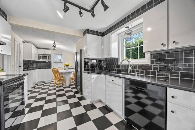 kitchen with black appliances, a sink, healthy amount of natural light, dark countertops, and vaulted ceiling