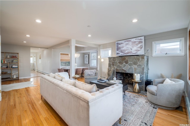 living area with light wood-style flooring, a stone fireplace, recessed lighting, and a baseboard radiator