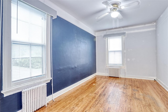 unfurnished room with radiator, wood finished floors, ceiling fan, and baseboards