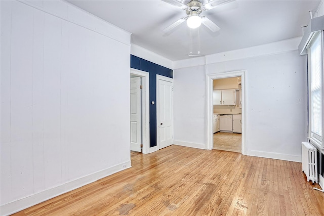 unfurnished bedroom featuring radiator heating unit, light wood-type flooring, baseboards, connected bathroom, and multiple windows