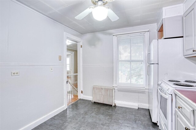 kitchen with radiator heating unit, white appliances, a ceiling fan, white cabinets, and baseboards
