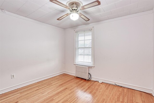 spare room featuring radiator, wood finished floors, ceiling fan, and baseboards
