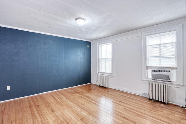 spare room with radiator heating unit, light wood-style floors, cooling unit, and baseboards
