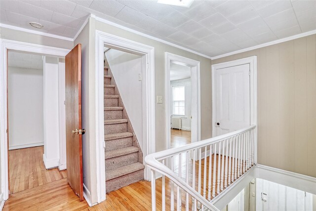 stairs with crown molding and wood finished floors