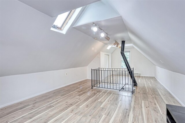 additional living space with a skylight, vaulted ceiling, wood finished floors, a baseboard radiator, and baseboards