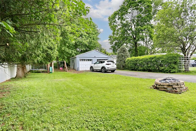 view of green lawn with an outdoor fire pit and a detached garage