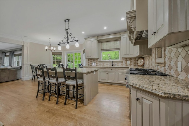 kitchen with a kitchen breakfast bar, light wood-type flooring, a chandelier, light stone countertops, and tasteful backsplash