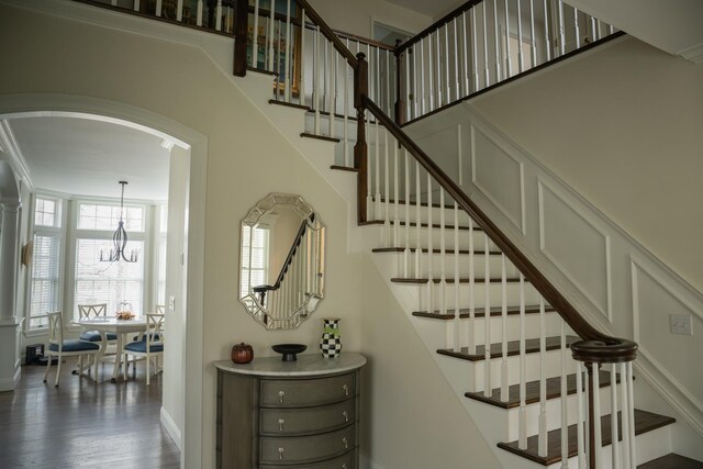 staircase featuring a chandelier, wood finished floors, baseboards, and arched walkways