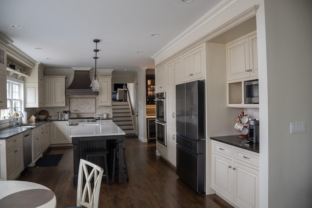 kitchen with appliances with stainless steel finishes, a sink, custom range hood, a center island with sink, and decorative backsplash