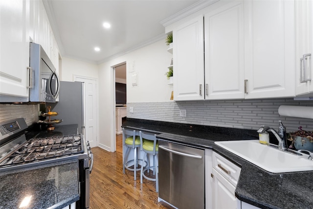 kitchen with appliances with stainless steel finishes, dark countertops, a sink, white cabinetry, and crown molding