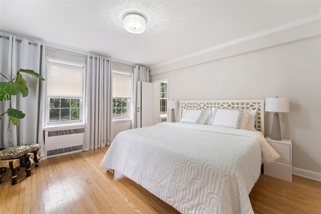 bedroom featuring radiator heating unit, light wood finished floors, crown molding, and baseboards