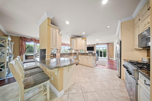 9 Fairwind Ct, Oakdale, NY 11769 - kitchen with appliances with stainless steel finishes, cream cabinetry, a peninsula, crown molding, and dark stone countertops