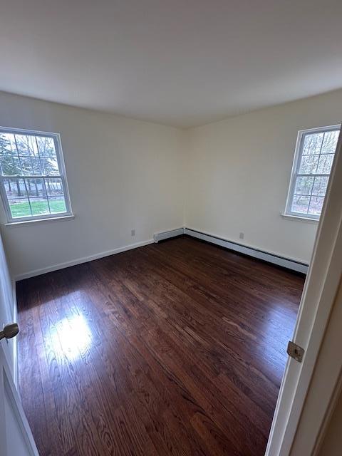 spare room with plenty of natural light, a baseboard heating unit, dark wood-style flooring, and baseboards