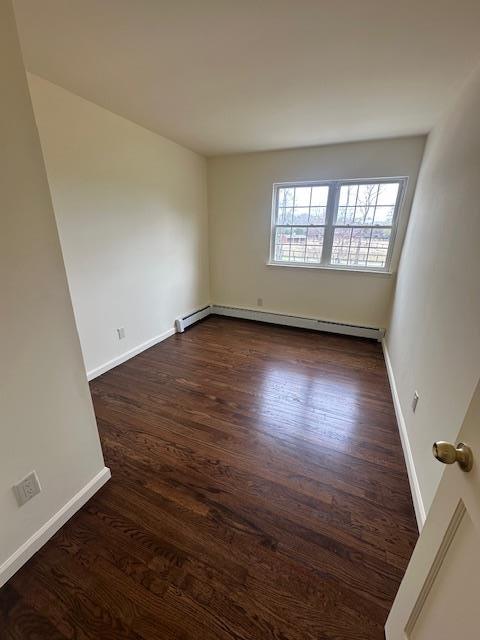 empty room with baseboard heating, dark wood-type flooring, and baseboards
