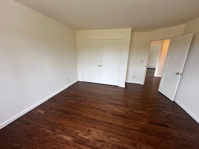 unfurnished bedroom featuring baseboards, dark wood finished floors, and a closet