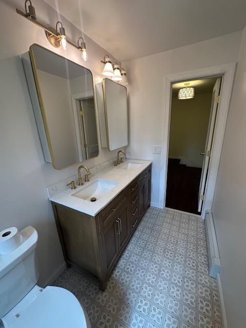 bathroom with toilet, a baseboard radiator, double vanity, and baseboards