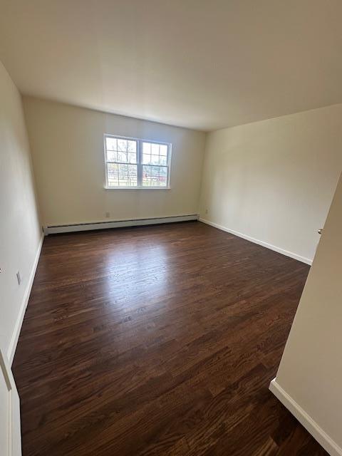 spare room with a baseboard heating unit, dark wood-style floors, and baseboards