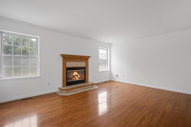 unfurnished living room with wood-type flooring, a tiled fireplace, baseboards, and crown molding