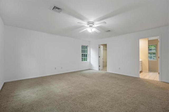 empty room with light colored carpet, a ceiling fan, and baseboards