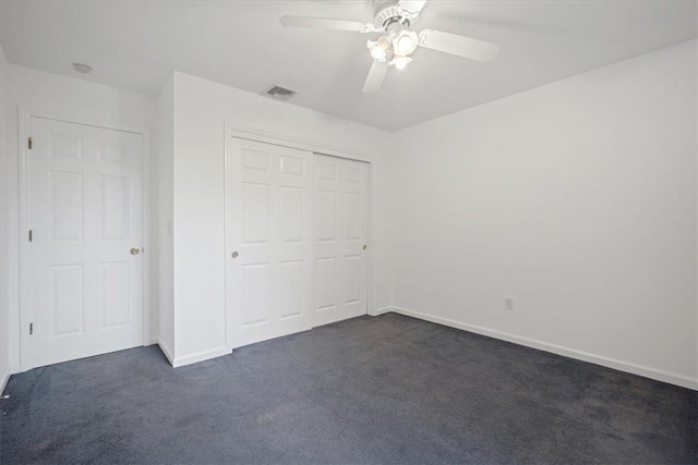 unfurnished bedroom featuring dark colored carpet, a closet, baseboards, and a ceiling fan