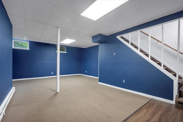 below grade area with a baseboard heating unit, a paneled ceiling, baseboards, stairway, and carpet