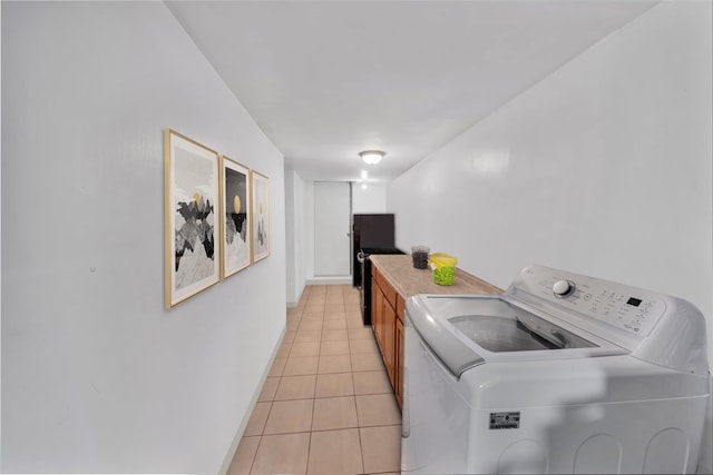 laundry area featuring washing machine and dryer, light tile patterned floors, cabinet space, and baseboards