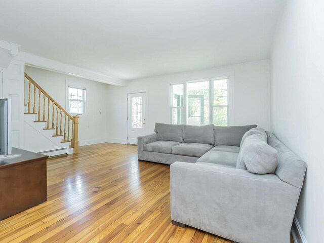 living room with a baseboard heating unit, stairs, light wood-type flooring, and baseboards