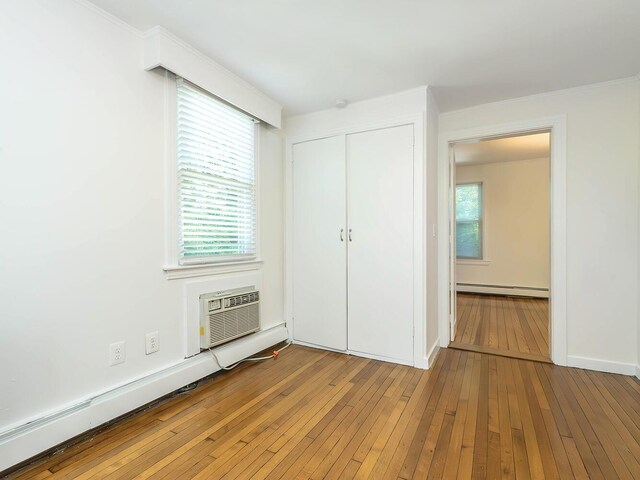 unfurnished bedroom with an AC wall unit, baseboard heating, hardwood / wood-style floors, a closet, and a baseboard radiator
