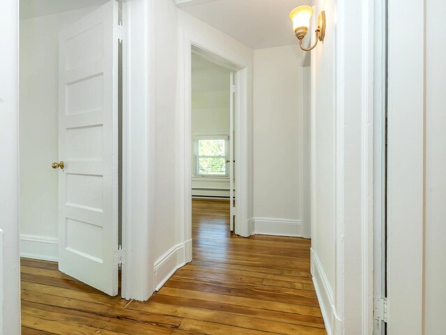 hall featuring a baseboard radiator, wood-type flooring, and baseboards