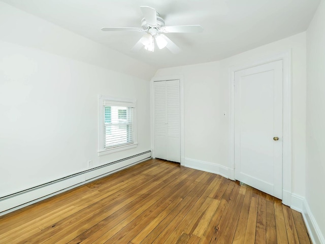 unfurnished bedroom with a baseboard radiator, hardwood / wood-style flooring, a closet, baseboards, and a ceiling fan