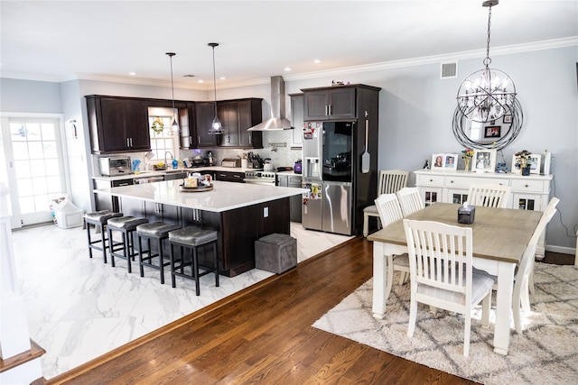 kitchen featuring stainless steel appliances, wall chimney exhaust hood, a kitchen island, light countertops, and dark brown cabinets