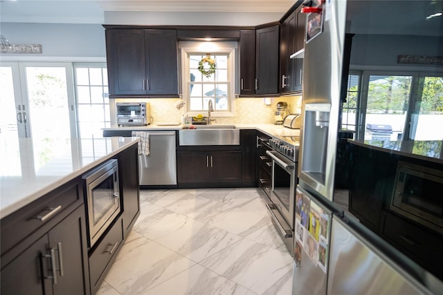 kitchen with stainless steel appliances, crown molding, a sink, light marble finish floors, and tasteful backsplash
