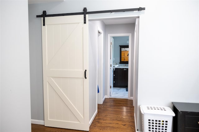 corridor featuring wood finished floors, a barn door, and baseboards