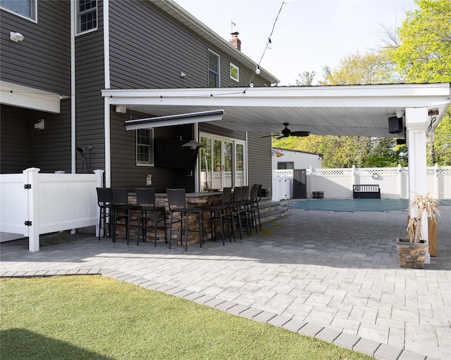 view of patio / terrace with ceiling fan, fence, and an outdoor bar