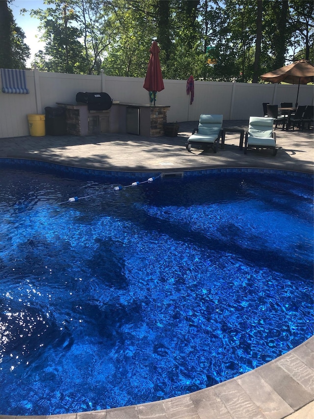 view of pool featuring exterior kitchen, fence, and a patio