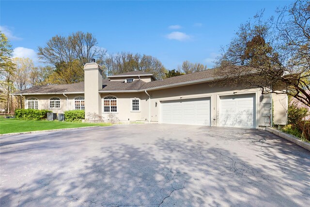 406 Duck Pond, Locust Valley, NY 11560 - view of front of house with asphalt driveway, stucco siding, an attached garage, and a chimney