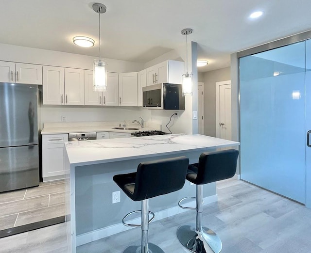 kitchen with appliances with stainless steel finishes, light stone counters, white cabinets, a kitchen bar, and a sink