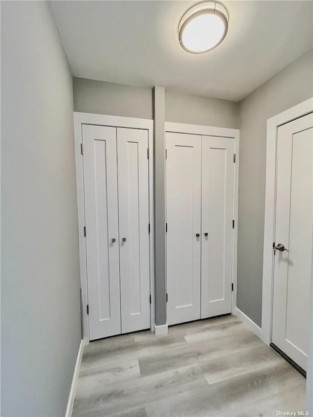 unfurnished bedroom featuring baseboards, light wood finished floors, and two closets
