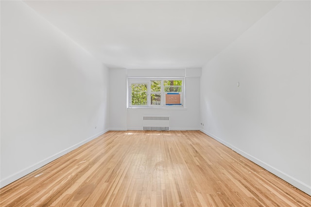 unfurnished room with radiator heating unit, light wood-style flooring, and baseboards