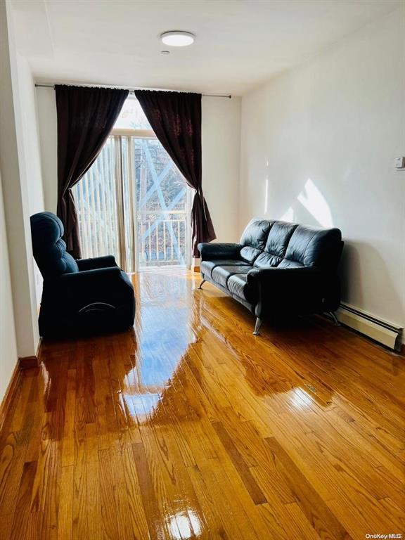 sitting room with a baseboard heating unit, hardwood / wood-style flooring, and baseboards