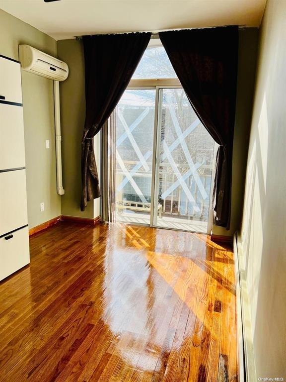 unfurnished living room with an AC wall unit, wood finished floors, and baseboards