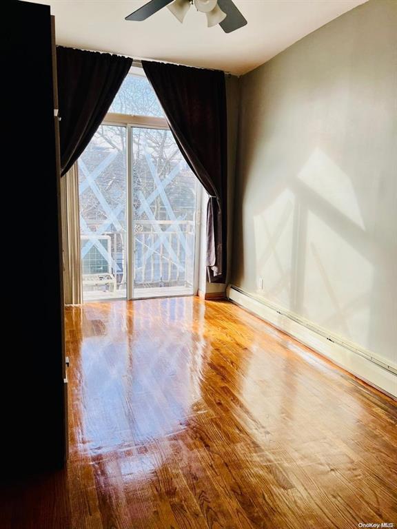 empty room featuring ceiling fan, wood finished floors, baseboard heating, and baseboards