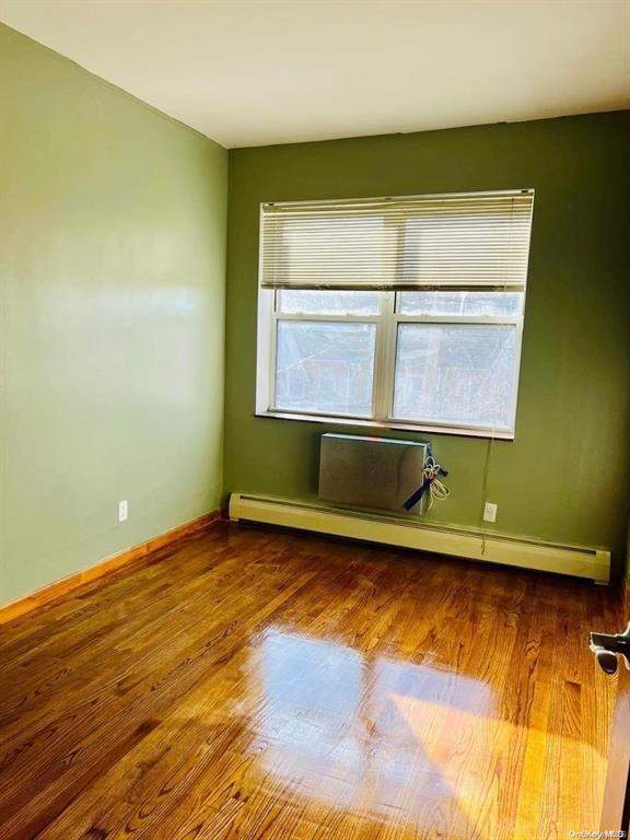 empty room with a baseboard heating unit, wood finished floors, and baseboards